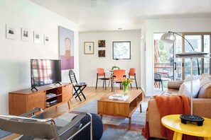 A modern living room with a sofa, coffee table, TV, and a dining area with chairs and a table.