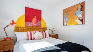 Une chambre à coucher avec un lit, une table de chevet, une lampe rouge et deux tableaux accrochés au mur.