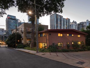 Eine moderne Straßenszene in der Stadt mit einer Mischung aus Wohn- und Geschäftsgebäuden, darunter ein markantes Ziegelgebäude mit großen Fenstern und flachem Dach.