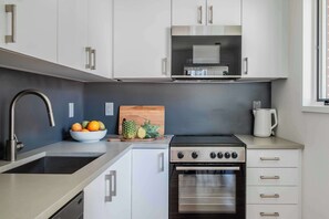 A modern kitchen with stainless steel appliances, a sink, and a bowl of fruit on the counter.