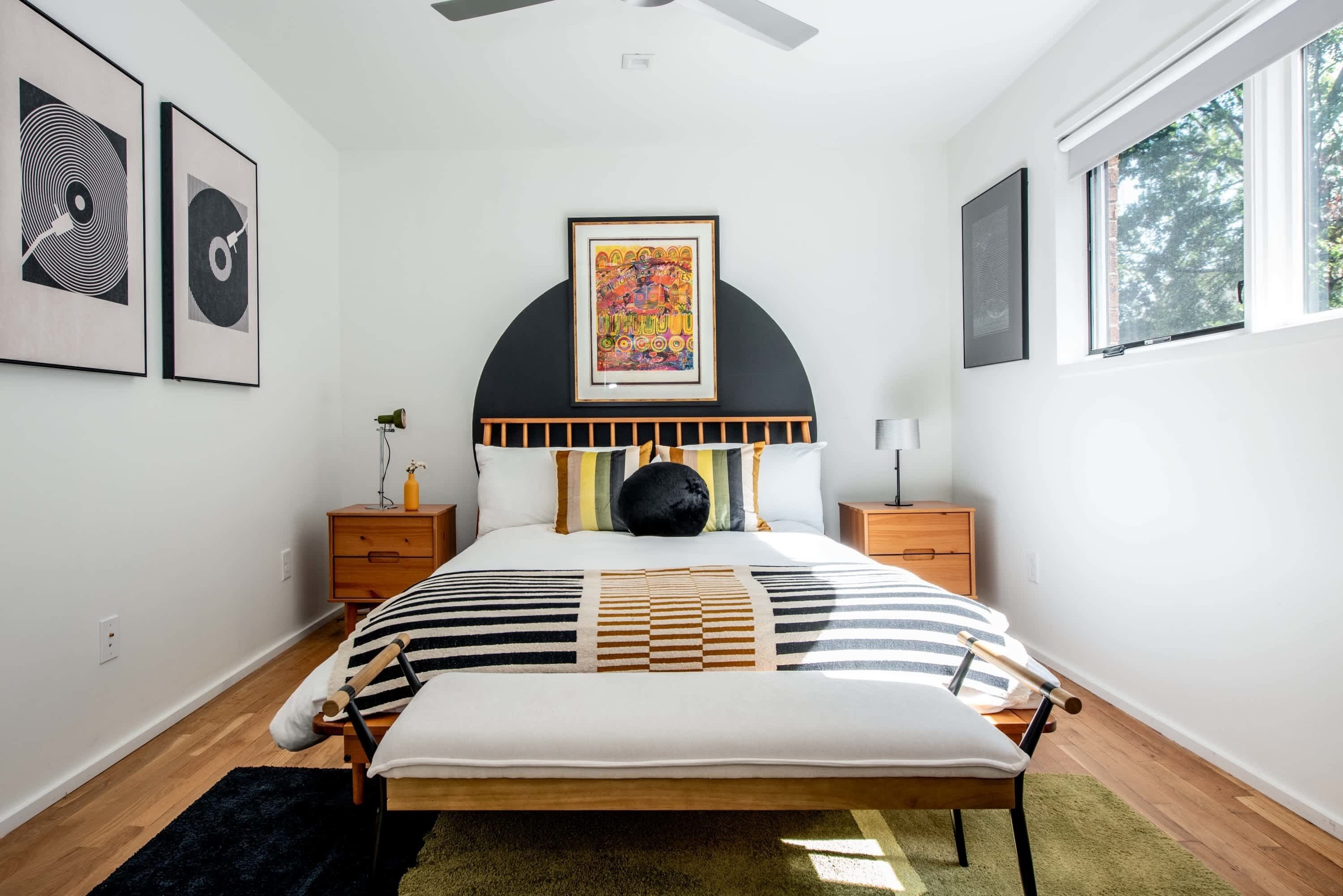 A modern bedroom with a bed, nightstands, a large window, and artwork on the walls.