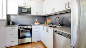 A modern kitchen with white cabinets, stainless steel appliances, and a wooden floor. - Modern Marvels (Atlanta)