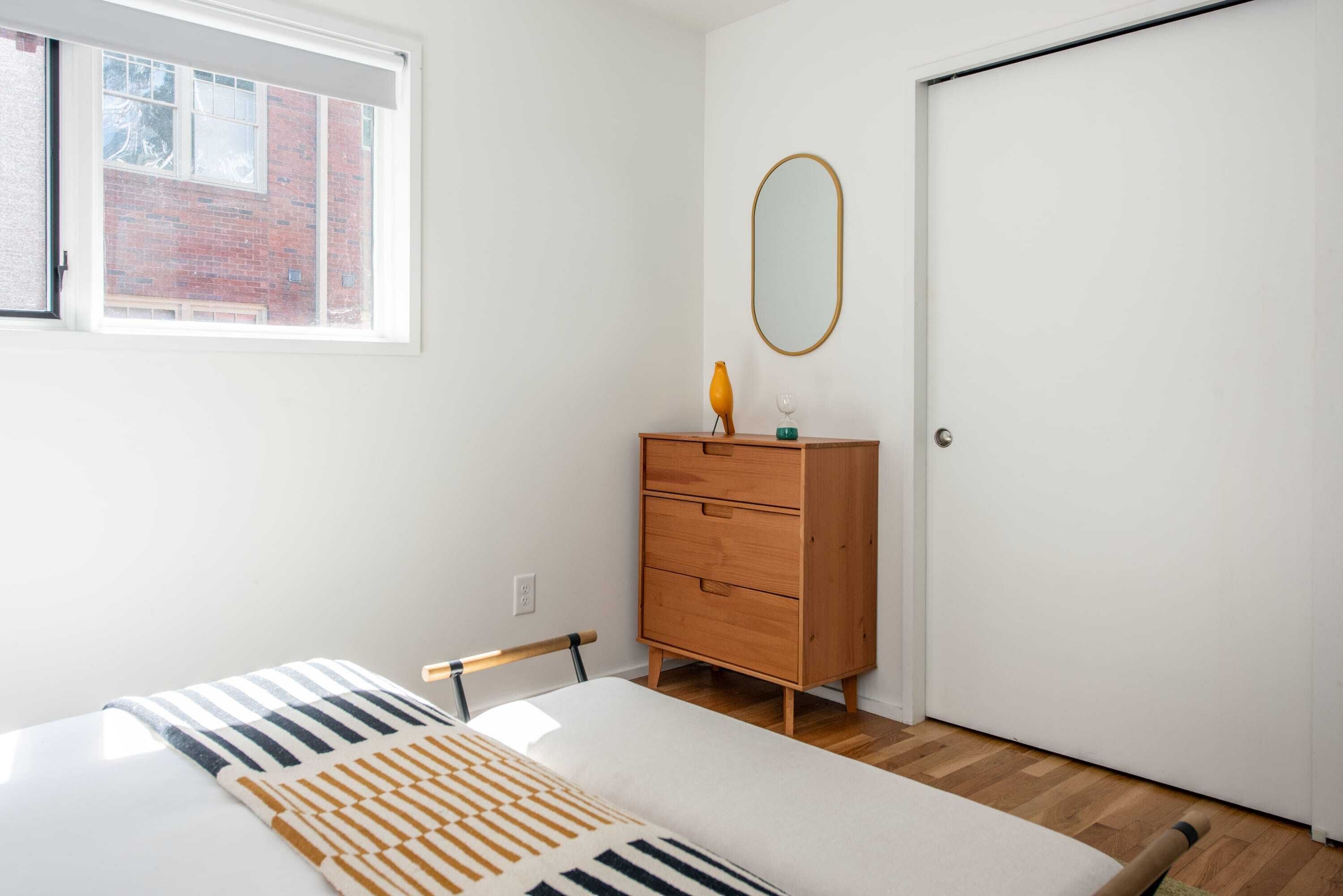 A bedroom with a bed, a dresser, a mirror, and a window.