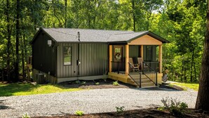 A cabin with a porch, a small deck, and a gravel driveway.