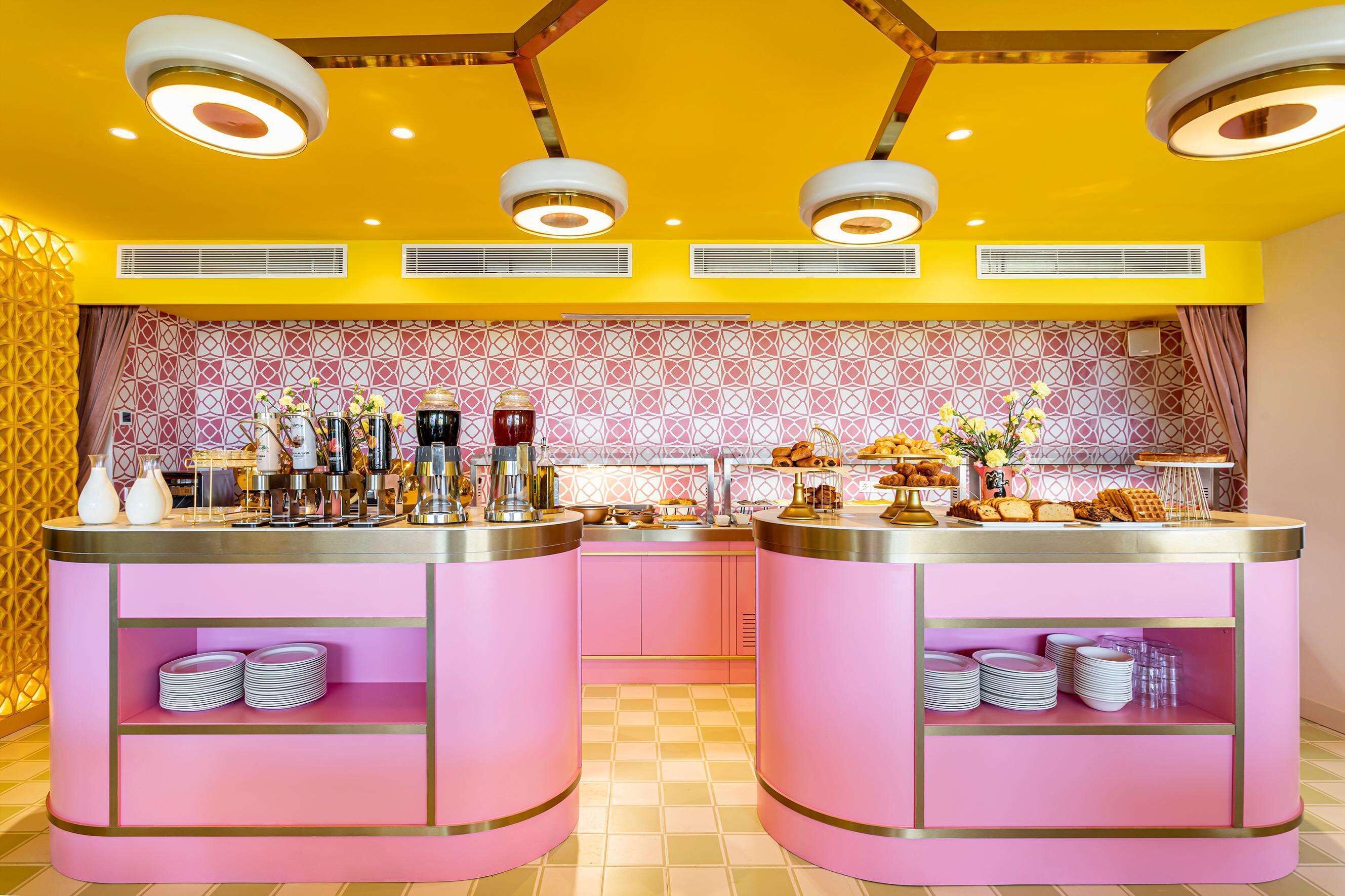 A brightly lit kitchen area with pink cabinetry, a checkered floor, and a patterned backsplash.