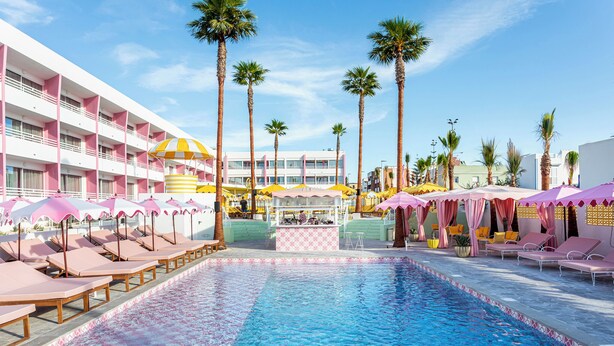 Een zwembadgedeelte van een hotel met ligbedden, parasols en een bar.
