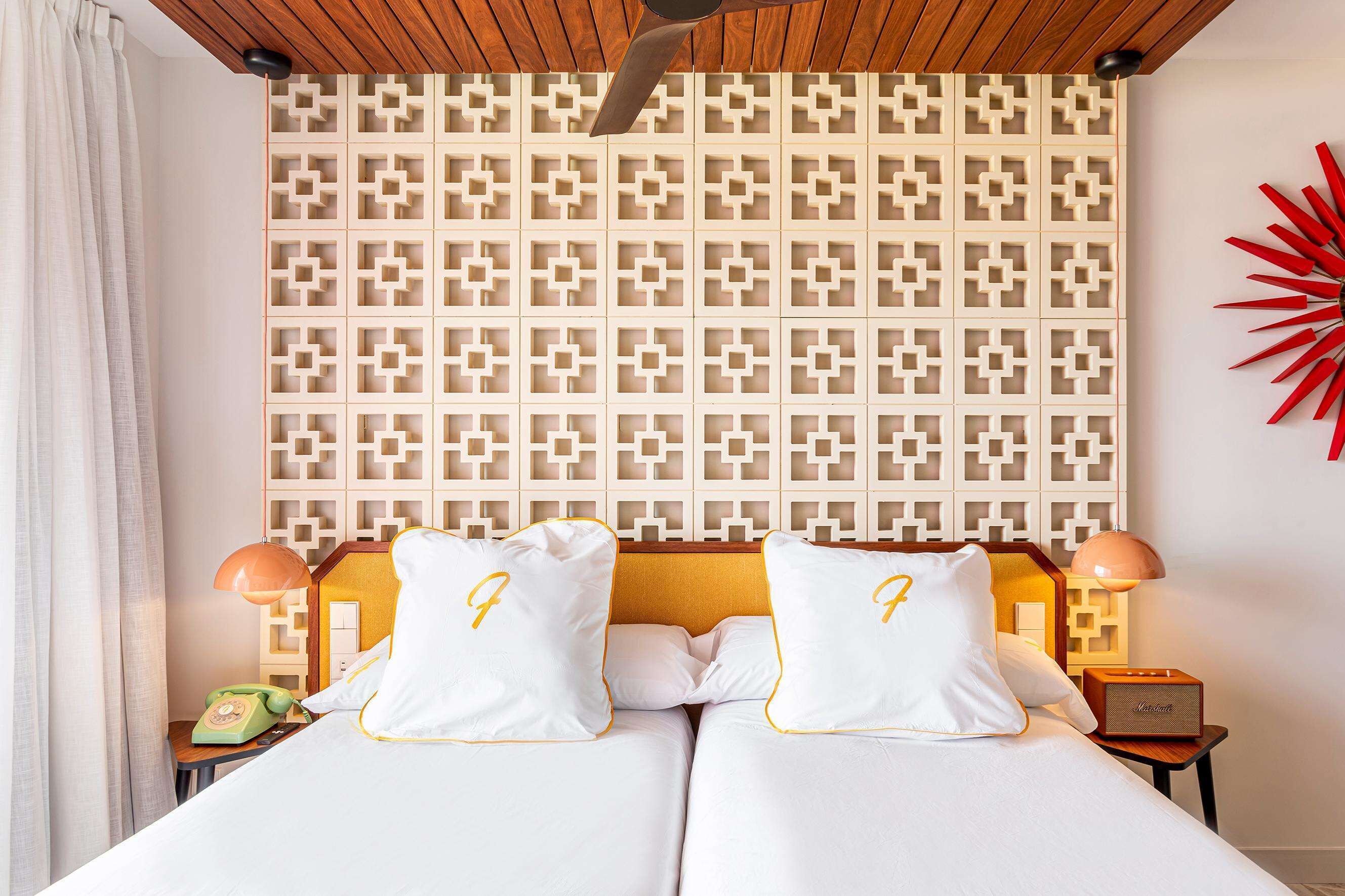 A hotel room with a patterned wall, two beds with matching pillows, a telephone, and a bedside lamp.