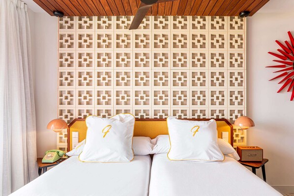Une chambre d’hôtel avec un mur décoré de motifs, deux lits avec des oreillers assortis, un téléphone et une lampe de chevet.