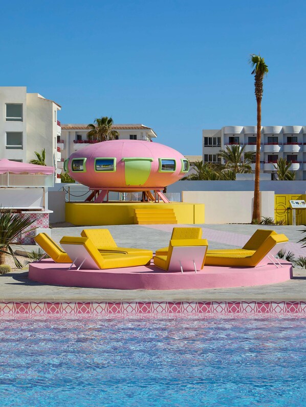 A pool area with yellow lounge chairs and a pink and green structure resembling a submarine. - Los Felices Ibiza (Sant Josep de sa Talaia)
