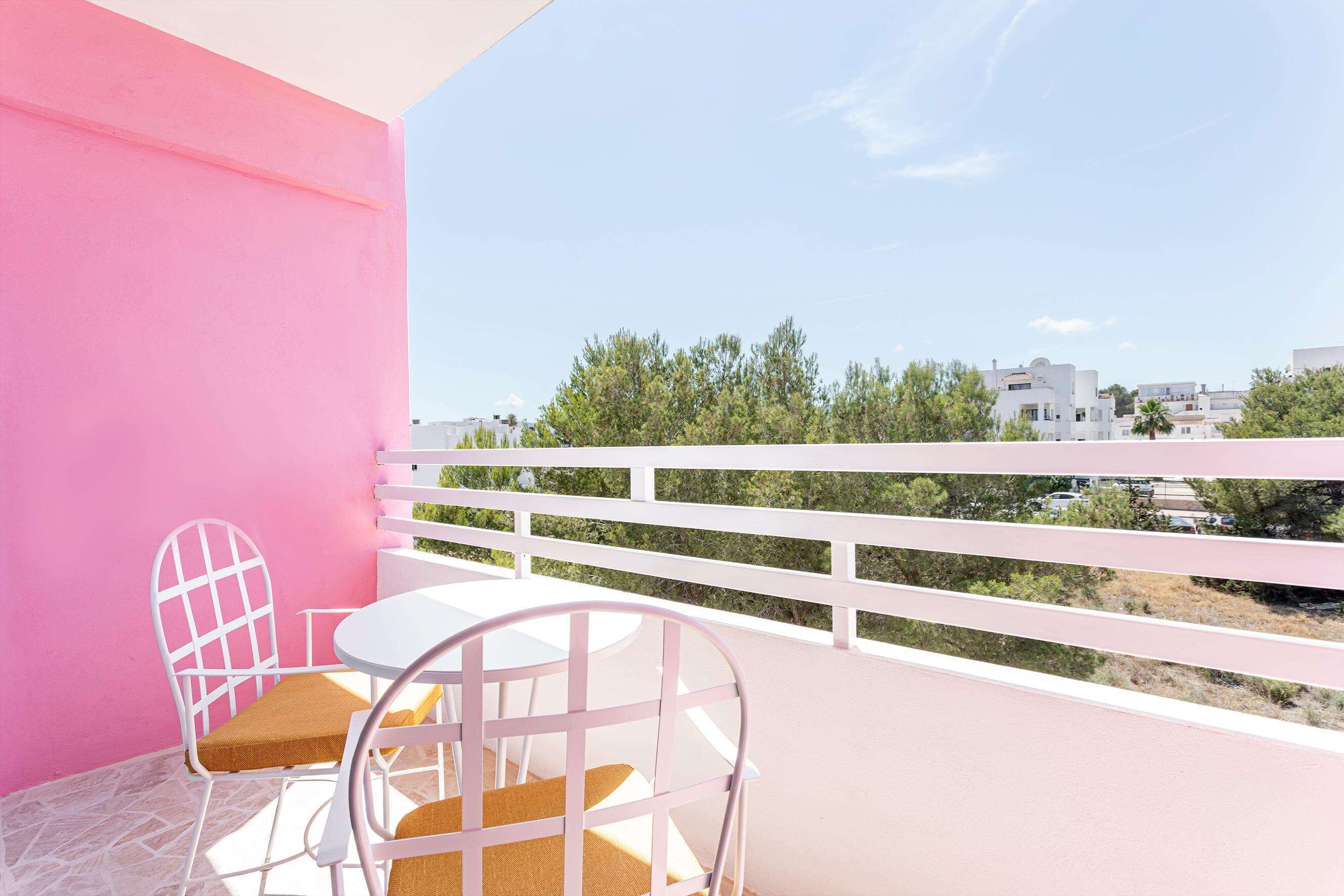 A balcony with a white railing, a white table, and two white chairs with brown cushions.