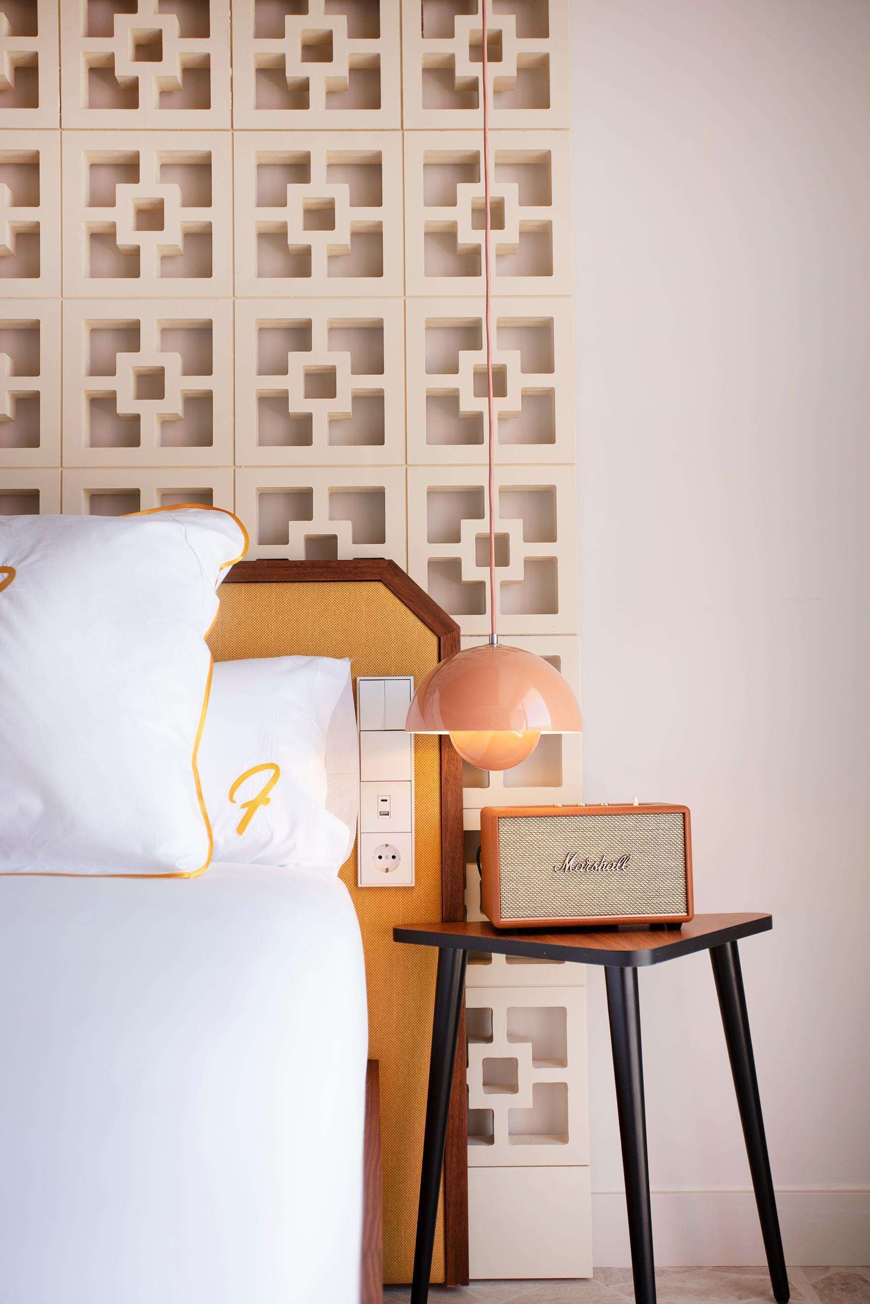 A neatly arranged hotel room with a bed, a nightstand, a lamp, and a speaker.