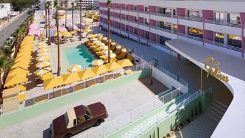 A hotel with a swimming pool, yellow umbrellas, and a red car parked outside.