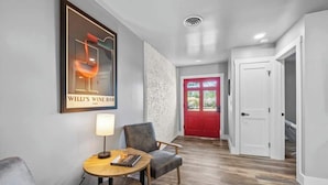 A modern interior with a framed poster, a round table with a lamp, a grey armchair, and a red door.