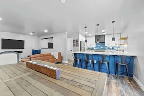 A modern living room with a wooden coffee table, a brown sofa, and a kitchen area with blue bar stools.