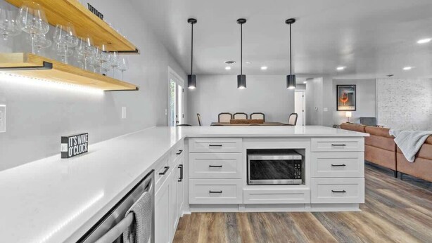 A modern kitchen with white cabinetry, a built-in oven, pendant lighting, and a wine rack.