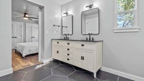 A bathroom with a white vanity, two mirrors, a window, and a hexagonal tile floor.