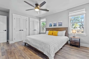A bedroom with a bed, a ceiling fan, a nightstand, and a window with a view.