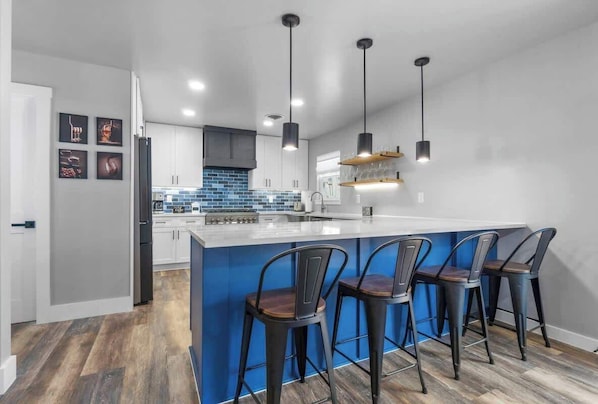 A modern kitchen with a central island, bar stools, pendant lighting, and a backsplash.
