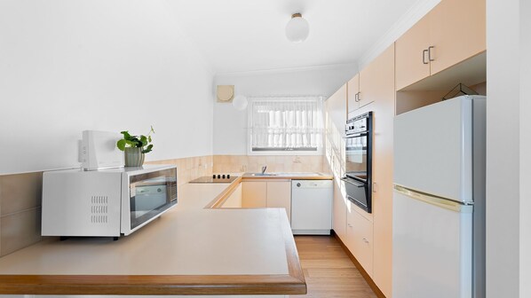 A modern kitchen with white appliances, a wooden countertop, and a window with sheer curtains.