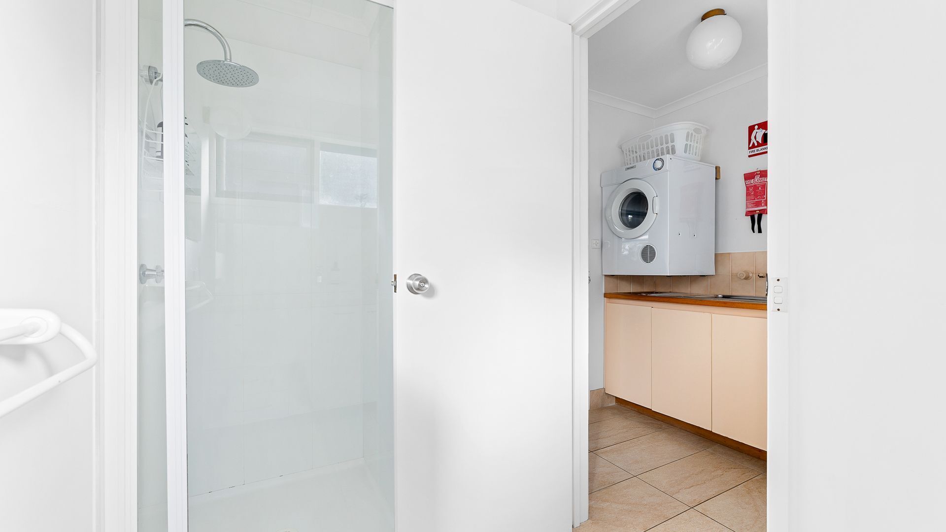 A modern bathroom with a glass shower enclosure, a white toilet, and a visible laundry area with a washing machine and dryer.