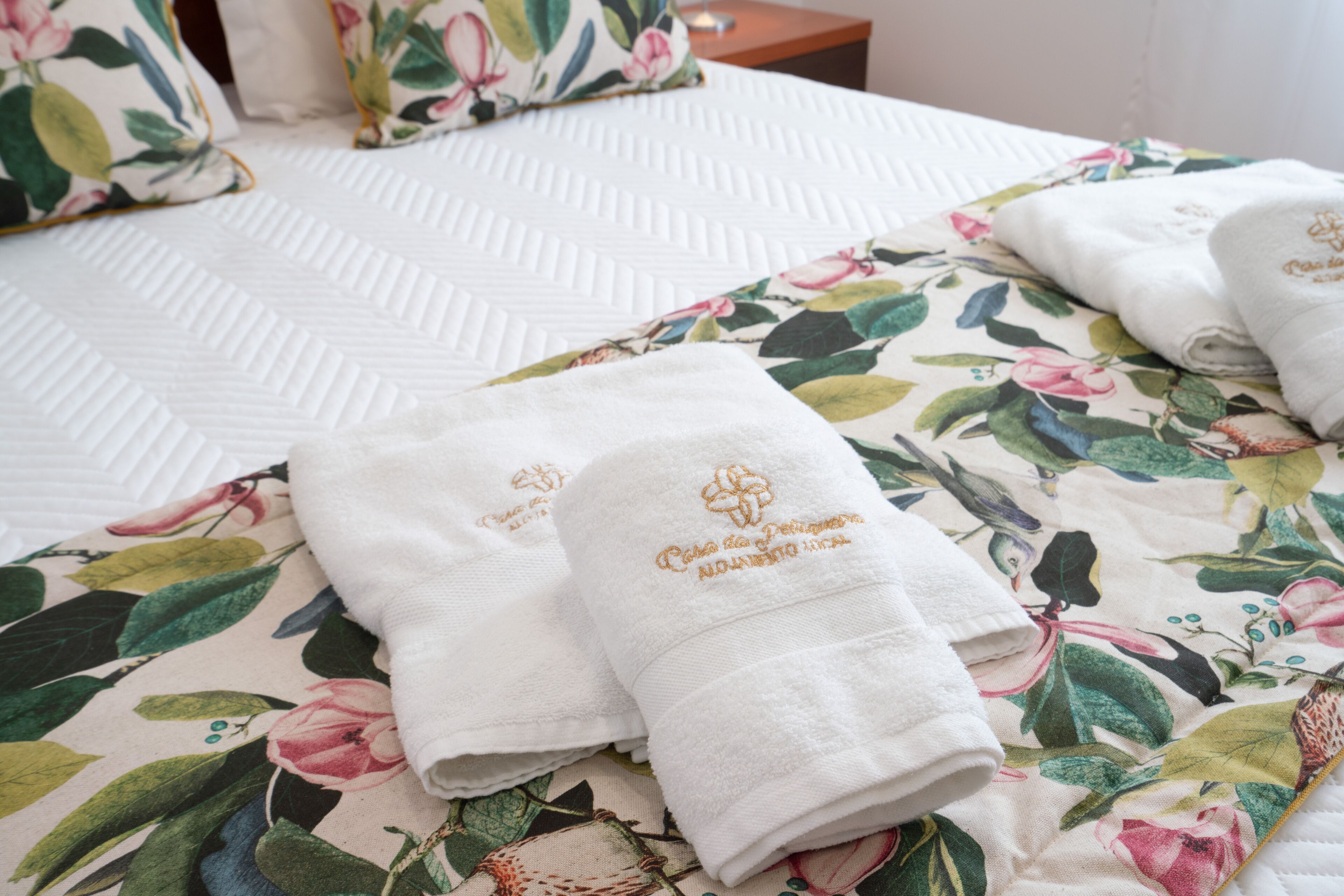 Un letto rifatto con cura, con una coperta a motivi floreali e due asciugamani piegati con ricami.