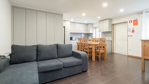 A modern living room with a grey sofa, a wooden dining table with chairs, and a kitchen area in the background. - Casa da Petisqueira 88, Paredes - O Porto  (Paredes)