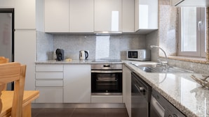 A modern kitchen with white cabinets, a granite countertop, a built-in oven, a microwave, and a stainless steel sink. - Casa da Petisqueira 88, Paredes - O Porto  (Paredes)