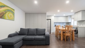 A modern living room with a grey sectional sofa, a dining area with wooden chairs, and a kitchen with white cabinets and a washing machine. - Casa da Petisqueira 88, Paredes - O Porto  (Paredes)