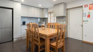 A modern kitchen with white cabinets, a stainless steel refrigerator, a wooden dining table with chairs, and a granite countertop.