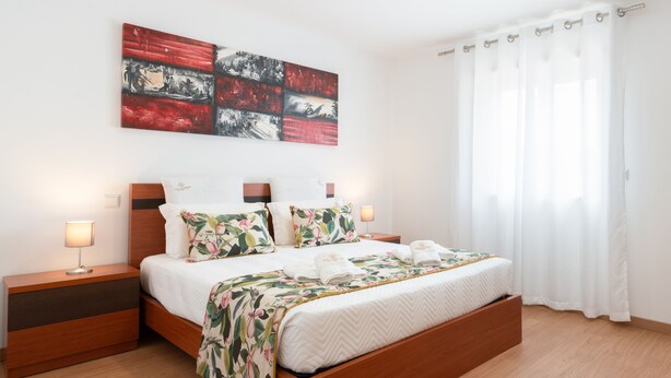 A modern bedroom with a wooden bed, a nightstand with a lamp, and a large abstract painting on the wall. - Casa da Petisqueira 88, Paredes - O Porto  (Paredes)