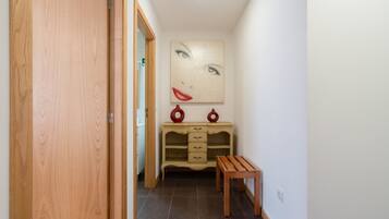 Un couloir avec une porte en bois, un banc, un meuble de couleur crème doté de tiroirs et un grand tableau accroché au mur.