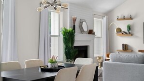 A modern dining area with a black table and white chairs, a decorative light fixture, and a grey sofa in the background.