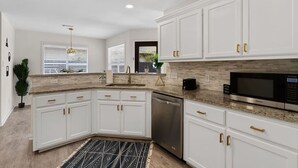A modern kitchen with white cabinets, granite countertops, stainless steel appliances, and a black and white patterned rug.