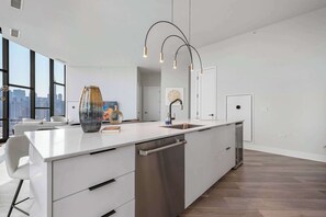 A modern kitchen with a large island, a dishwasher, and pendant lighting.