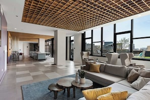 A spacious living area with a modern design, featuring a large sofa, coffee table, and a view of the city through large windows.