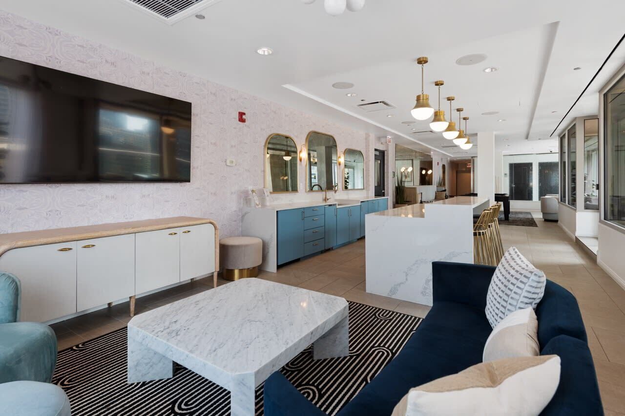 A modern hotel lobby with a marble coffee table, seating area, and a kitchen in the background.