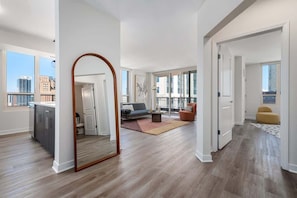 A spacious living area with a large mirror, a sofa, a coffee table, and a view of the city.