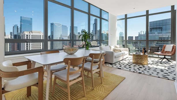A modern living room with a large window, a dining area with a table and chairs, and a seating area with a sofa and armchairs.