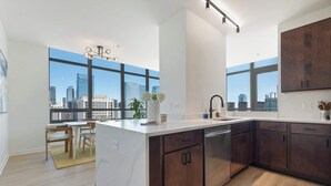 A modern kitchen with a large island, dark wood cabinets, and a view of the city skyline through large windows.