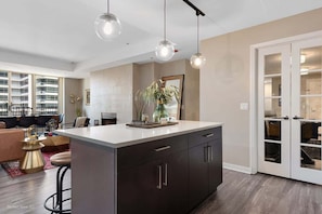 A modern kitchen with a central island, pendant lighting, and a view of the living area.