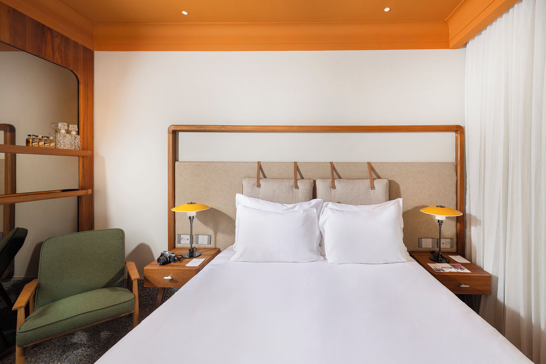 A hotel room with a large bed, two bedside tables, a green armchair, and a wooden headboard.