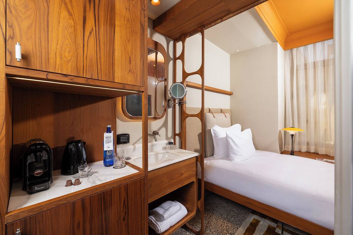 Ein Hotelzimmer mit einem Holzkasten, einem Waschbecken, einem Bett und einem Fenster mit Vorhängen.