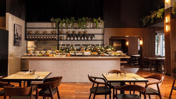 Un restaurant doté d’un bar central, de plusieurs espaces aménagés pour s’asseoir et d’une variété de plantes et de fleurs disposées sur des étagères.