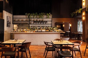 A restaurant with a central bar area, multiple seating arrangements, and a variety of plants and flowers displayed on shelves. - Hotel 1935 (Tel Aviv)