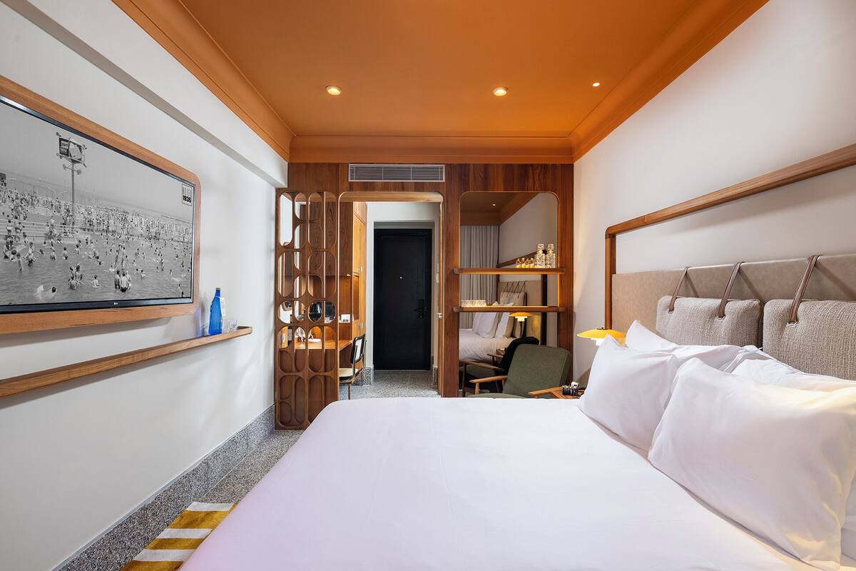 Ein Hotelzimmer mit einem großen Bett, einem Schreibtisch mit Stuhl, einem Kleiderschrank und einem Spiegel.
