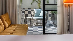 Une chambre d’hôtel comprenant un lit, un canapé, une table à manger avec des chaises, et donnant sur un balcon agrémenté de plantes.