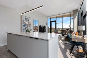 A modern kitchen with a large island, a dining area with a view, and a living space with a TV and artwork.