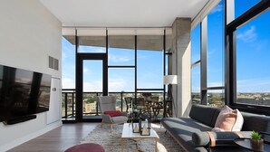 Ein modernes Wohnzimmer mit großem Fernseher, bequemen Sitzmöglichkeiten und Blick auf die Stadt.