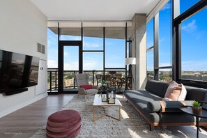 A modern living room with a large TV, comfortable seating, and a view of the city.