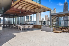 A rooftop terrace with a wooden pergola, outdoor seating, and a city skyline view.